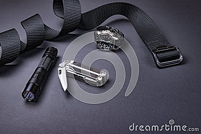 Everyday carry EDC items for men in black color - tactical belt, flashlight, watch and silver multi tool. Stock Photo