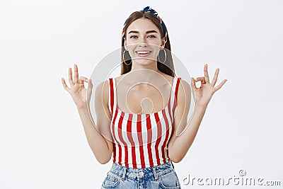 Everything fine, rely on me. Confident attractive young woman in striped top and headband showing okay gesture with both Stock Photo