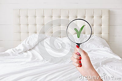 Everything in perfect and clean. Woman checks condition in hotel room, holds lens against white bed which demonstrates purity and Stock Photo