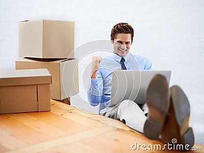 Everythings going my way. A young businessman surrounded by moving boxes celebrating while using a laptop. Stock Photo