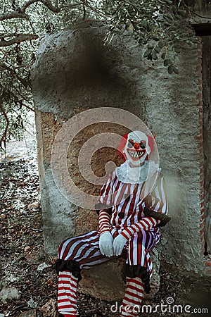 evil clown sitting in front of an old rustic house Stock Photo