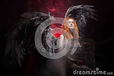 An evil tempting woman with large demon wings holds an Apple in a large cage and beckons to sin. Halloween photo plus Stock Photo