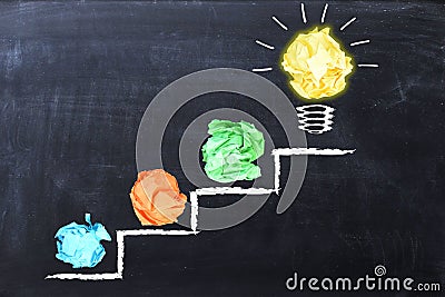 Evolving idea concept with colorful crumpled paper and light bulb on steps drawn on blackboard Stock Photo