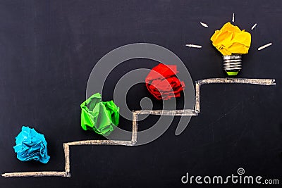 Evolving idea concept with colorful crumpled paper and light bulb on steps drawn on blackboard Stock Photo