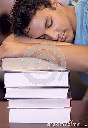 Exam time has gotten to him. A young student sleeping on his desk after a tiring study session. Stock Photo