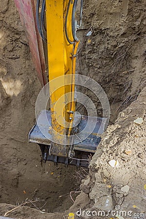 Excavator arm digging deep hole seeking cracked sewage pipe Stock Photo