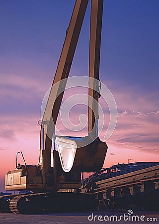 Excavator and barge waiting to be unloaded at harbor against twilight sky after sundown in vertical frame Stock Photo