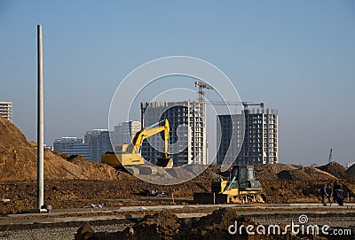 Excavator and bulldozer at a construction site on a background of a construction cranes and building. Editorial Stock Photo