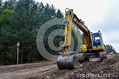 Excavator during construction new road in forest area. Yellow backhoe at groundwork. Earth-moving equipment fort road work, Stock Photo