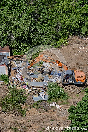 Excavator demolishes illegal buildings in the forest among green trees - Moscow, Russia, June 26, 2020 Editorial Stock Photo