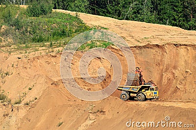 Excavator developing the sand on the opencast and loading it to the heavy dump truck. Editorial Stock Photo