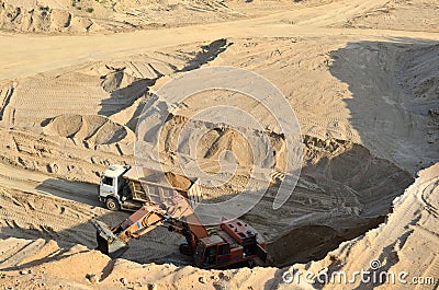 Excavator developing the sand on the opencast and loading it to the heavy dump truck. Processing of loose material in mining Editorial Stock Photo