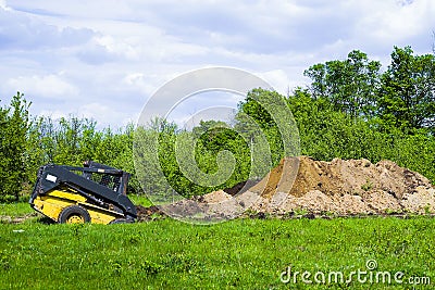 Excavator digging pit on grassy field with garden on background Stock Photo