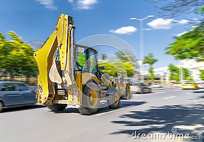 The excavator drives or goes fast on the street with heavy traffic with blue sky and green trees in background, Ankara, Turkey Stock Photo
