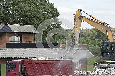 Excavator loads construction waste into a red truck. Destroyed concrete, construction waste. Stock Photo
