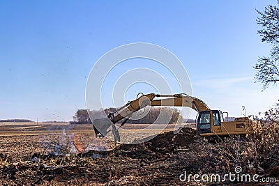 Excavator machinery moving trees and debris into a fire pit Stock Photo