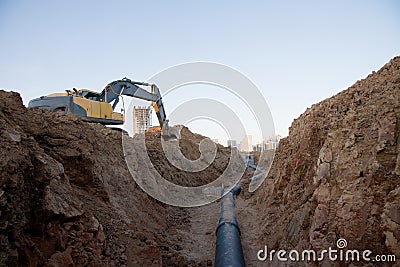 Excavator at work trenching at a construction site. Trench for laying external sewer pipes. Sewage drainage system for a multi- Stock Photo