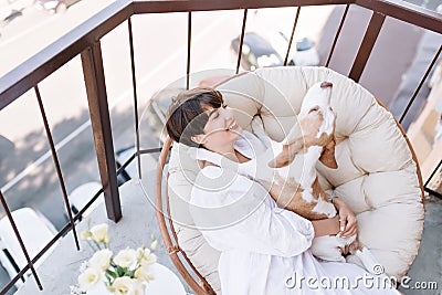 Excellent girl with charming smile enjoys Saturday morning on balcony holding funny beagle dog. Pretty lady with short Stock Photo