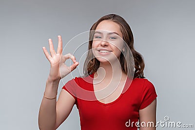 Excellent job. Attractive young brunette woman in red t shirt showing OK sign and smiling, give positive reply Stock Photo