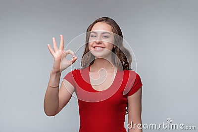 Excellent job. Attractive young brunette woman in red t shirt showing OK sign and smiling, give positive reply Stock Photo