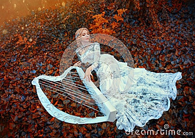 Excellent princess with blond hair in long lace vintage dress lies on red dark leaves, girl resting in autumn forest Stock Photo