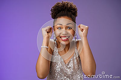 Excited african woman in elegant silver dress brilliants smiling thrilled winning clench raised fists grinning Stock Photo