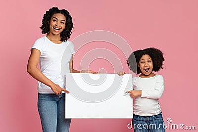 Excited Afro mother and daughter holding and pointing at white placard Stock Photo