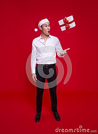 Excited asian business man wearing Santa hat and looking surprise with the falling gift box on hand. on over red background Stock Photo