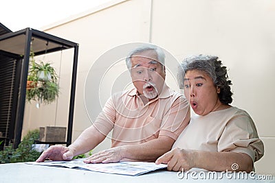 Excited Asian senior mature couple feeling amazed by good surprise news while reading newspaper . Stock Photo