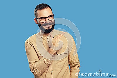 Excited bearded man smiling while pointing aside on empty space over blue Stock Photo