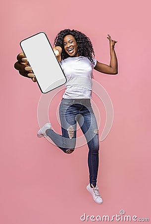 Excited black woman showing smarthone with blank white screen to camera, jumping with modern gadget, mockup Stock Photo