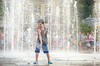 Excited boy having fun between water jets, in fountain. Summer i Stock Photo