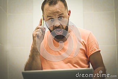 Excited businessman working on laptop and talking on phone seated on the toilet Stock Photo