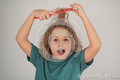 Excited child with curly blonde hair holding comb hairbrush for combing. Child with tangled blonde long hair tries to Stock Photo