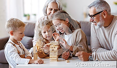 Excited children playing game Jenga at home with positive senior grandparents while sitting on sofa Stock Photo