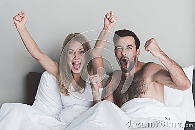 Excited couple celebrating victory of their team in bedroom Stock Photo