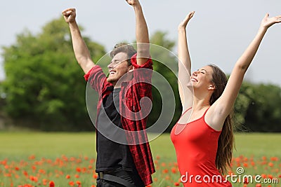 Excited couple raising arms on a poppy field Stock Photo