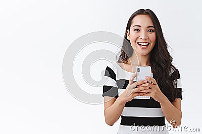 Excited, enthusiastic good-looking asian woman in casual outfit holding smartphone, thrilled smiling and looking camera Stock Photo