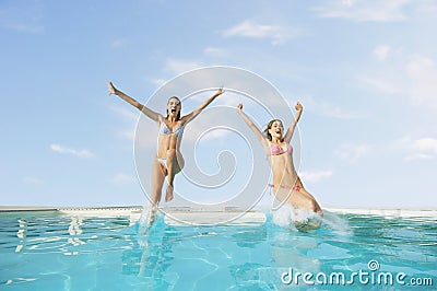 Excited Female Friends Jumping In Pool Stock Photo
