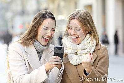 Excited friends reading phone content in winter Stock Photo