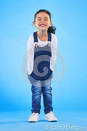 Excited girl child, fashion and studio portrait with jeans, dungaree and trendy style by blue background. Female kid Stock Photo