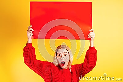 Excited girl dressed casual and glasses opened mouth in surprise and bulged eyes holding empty red signboard with your inscription Stock Photo