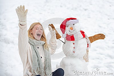 Excited girl plaing with a snowman on a snowy winter walk. Making snowman and winter fun. Cute snowman in hat and scalf Stock Photo