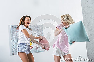 excited girls having pillow fight on bed Stock Photo