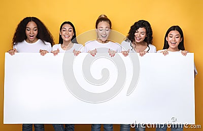 Excited Girls Holding Empty Poster For Text, Yellow Background, Mockup Stock Photo