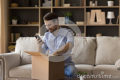 Happy young male open postal parcel make photo on phone Stock Photo