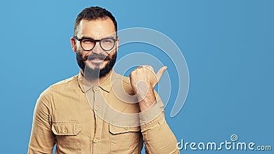 Excited hipster man points aside on empty space, isolated over blue wall Stock Photo