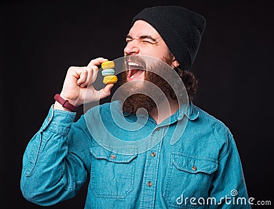 Excited and hungry bearded man is trying to eat three macaroons. Stock Photo