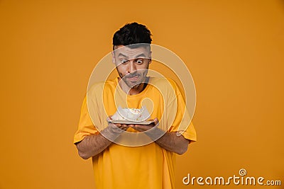 Excited hungry man holding cake and licking his lips isolated over yellow wall Stock Photo
