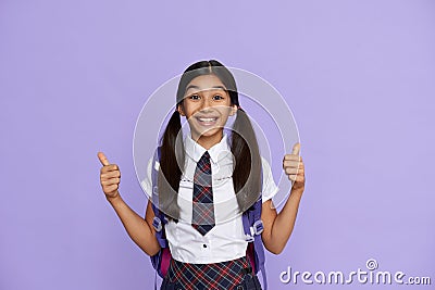 Excited happy indian school girl show thumbs up isolated on violet background. Stock Photo